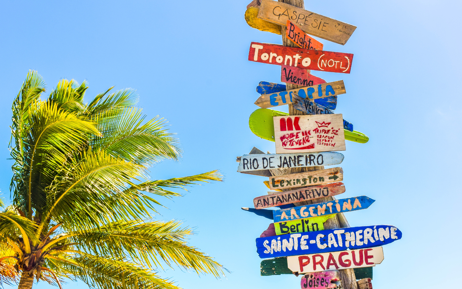 A imagem retrata uma composição vibrante e diversificada de várias placas alusivas a destinos turísticos ao redor do mundo. Cada placa exibe símbolos representativos de diferentes lugares, sugerindo uma variedade de culturas e experiências de viagem. Os designs podem incluir ícones famosos, marcos arquitetônicos distintos e elementos culturais específicos de cada região.  A disposição das placas cria um mosaico visualmente atraente, remetendo à ideia de um mundo globalizado e conectado através das viagens. 