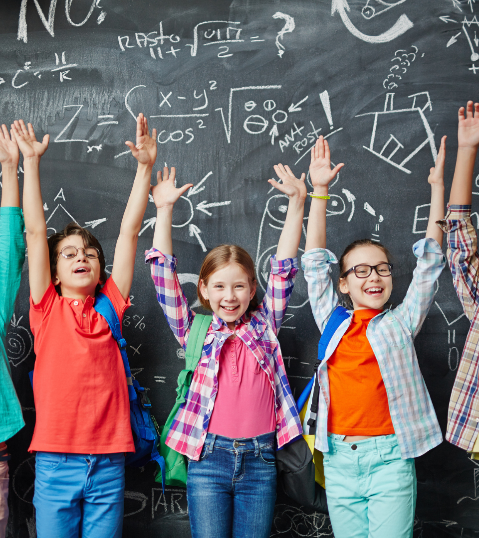 quatro meninos com os braços no ar numa sala de aula